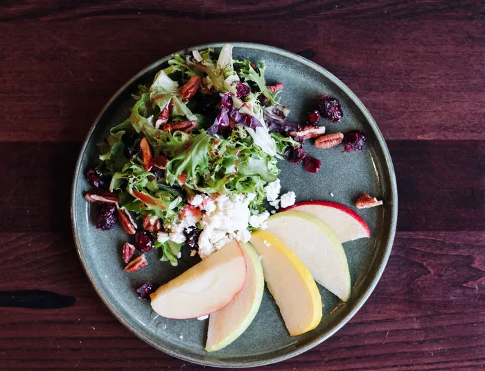 Greens with sliced apple, dried cranberries, pecans and goat cheese on a slate plate