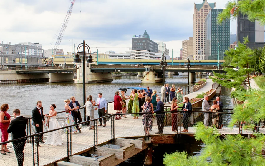 A wedding party and their guests on the Milwaukee Riverwalk with the downtown skyline behind them