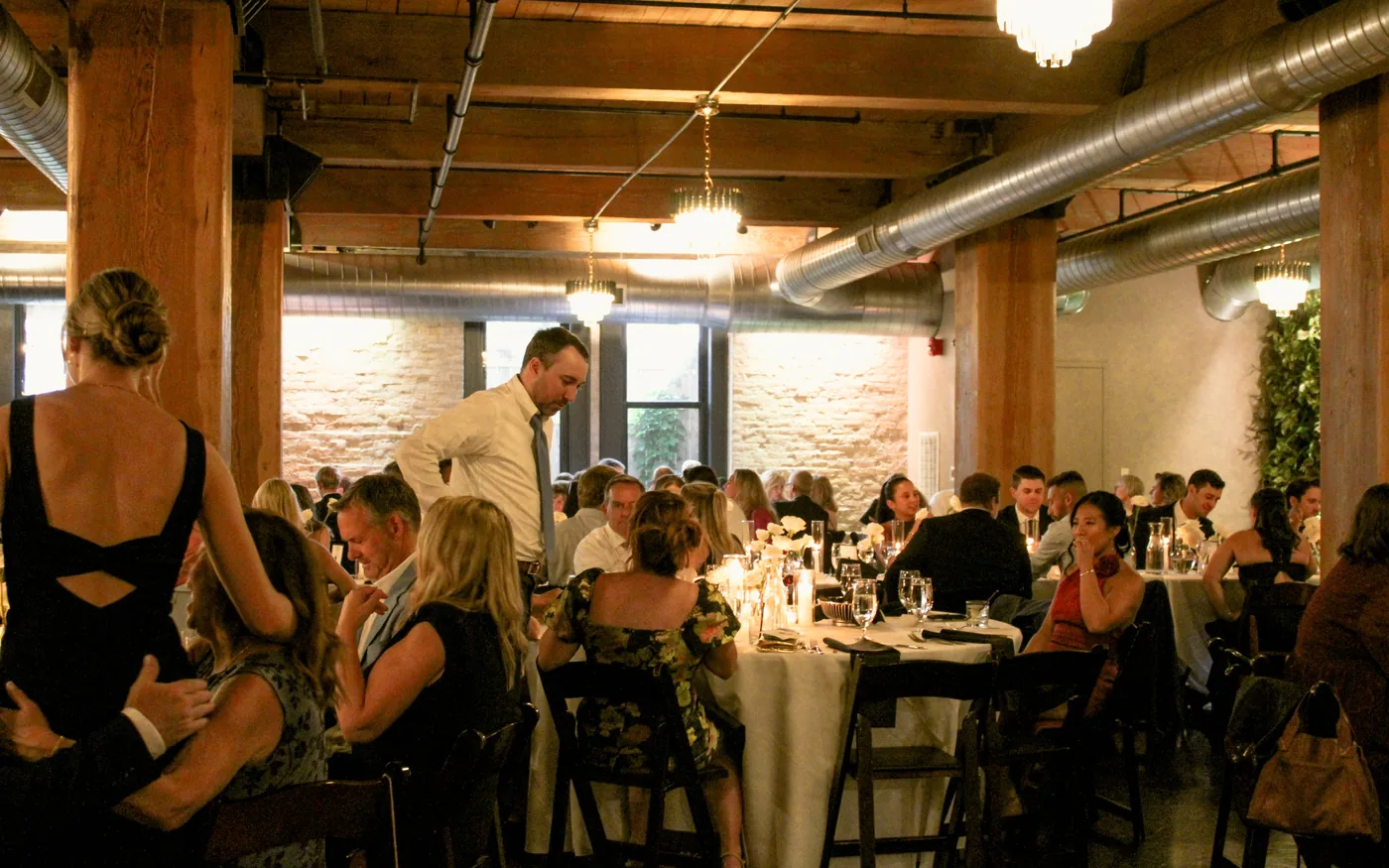 A seated dinner at round tables in a room with timber posts and exposed brick