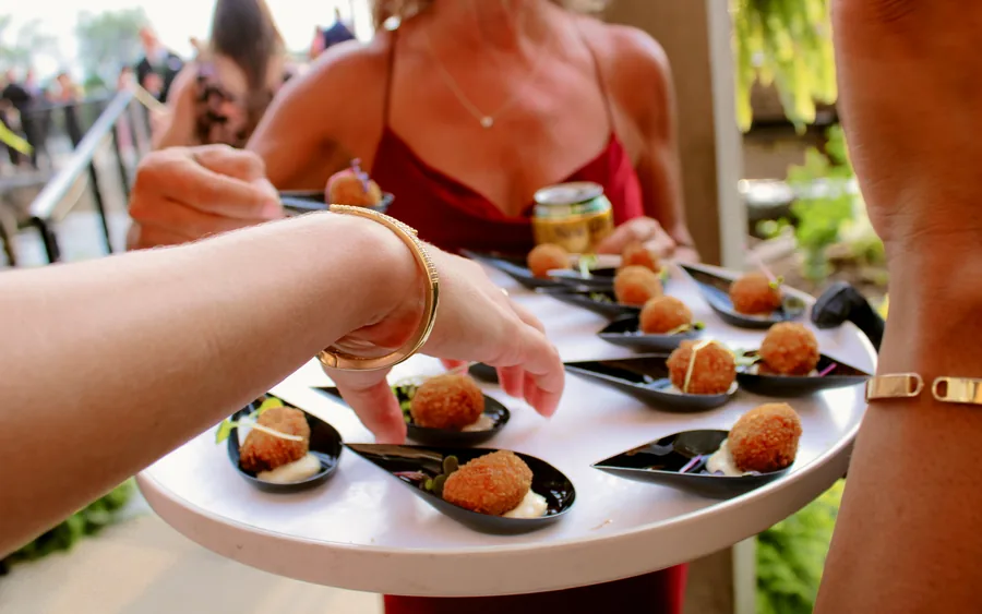 Hands reaching for arancini on a round passed tray at an outdoor party