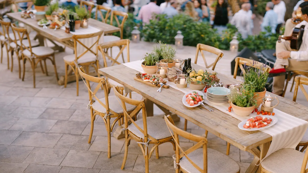 Long wooden tables set with shared boards, herbs in pots and plates, outdoors