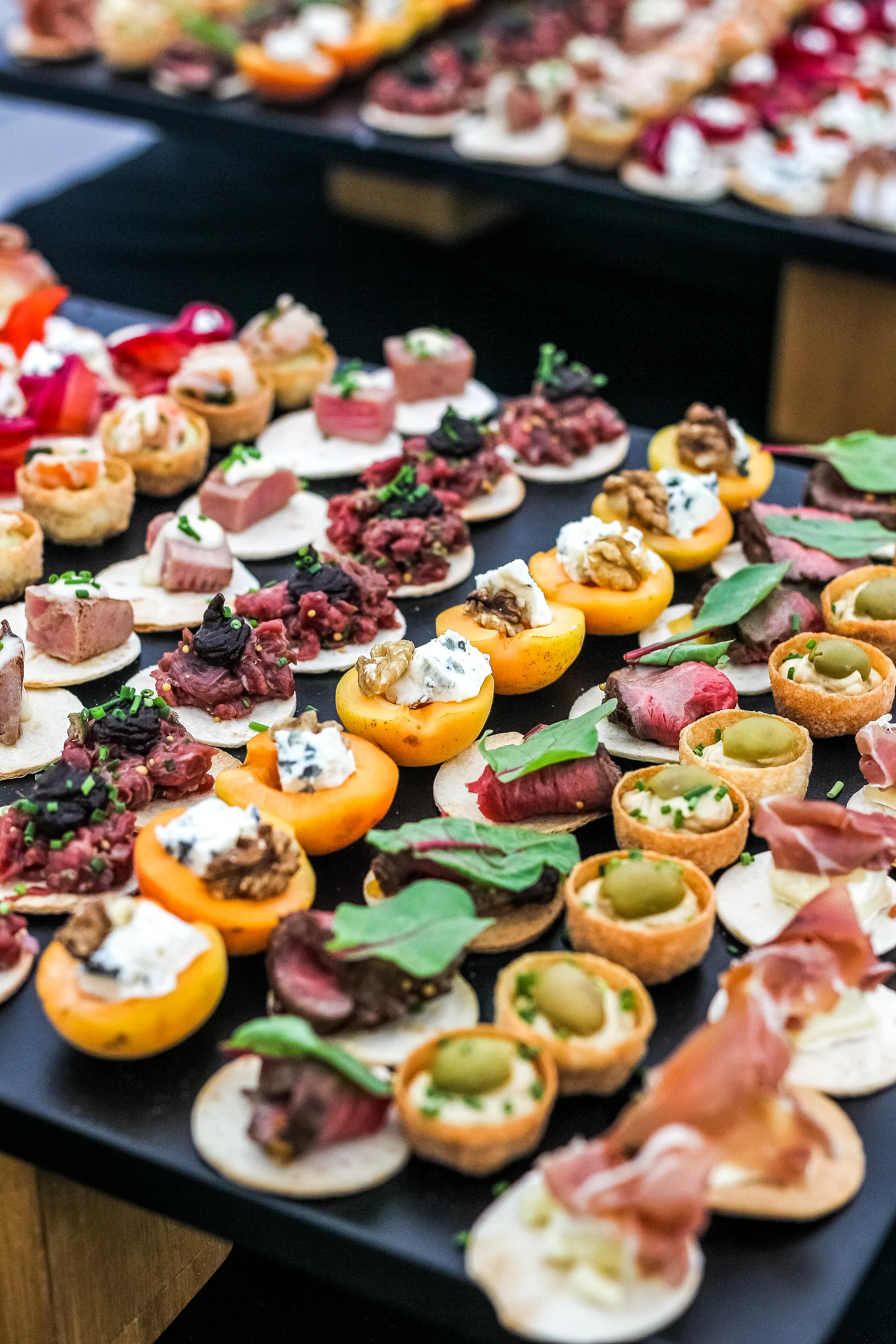 Hors d&rsquo;oeuvres prepared for passed service, dozens of bites laid out on a black tray