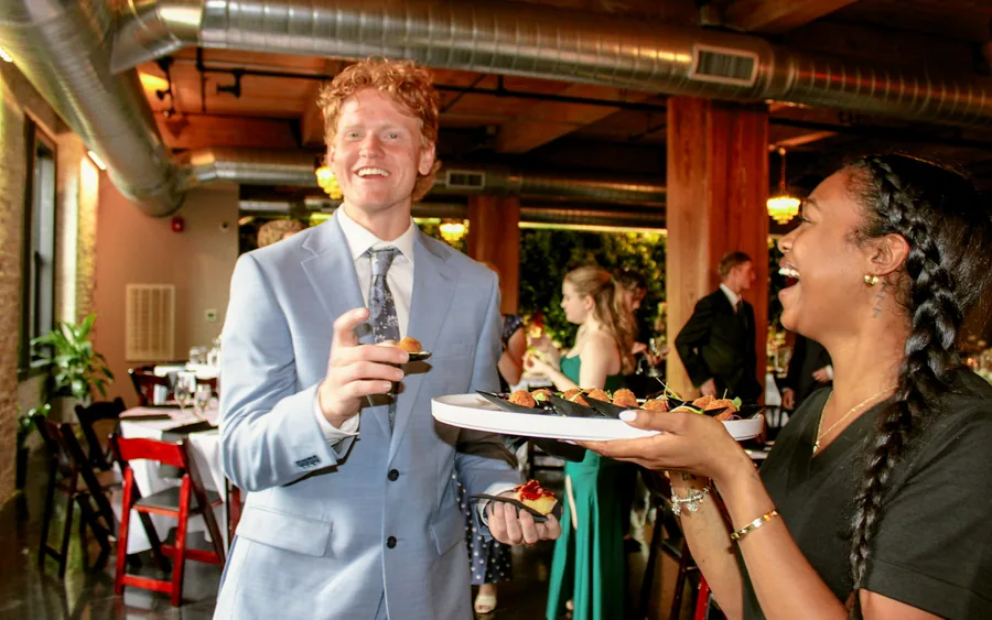 A server offering a tray of passed hors d&rsquo;oeuvres to a laughing guest at a wedding reception