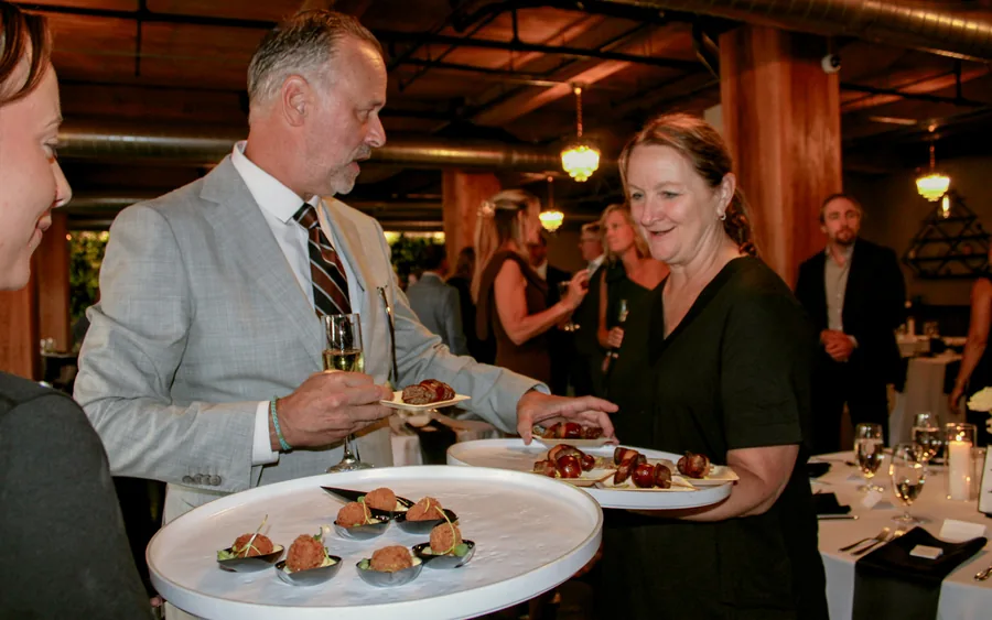 A server holding a tray of bacon-wrapped bites at a reception